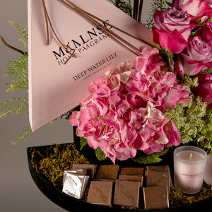 A chocolate tray with a box containing a diffuser and candle, decorated with various types of pink flowers