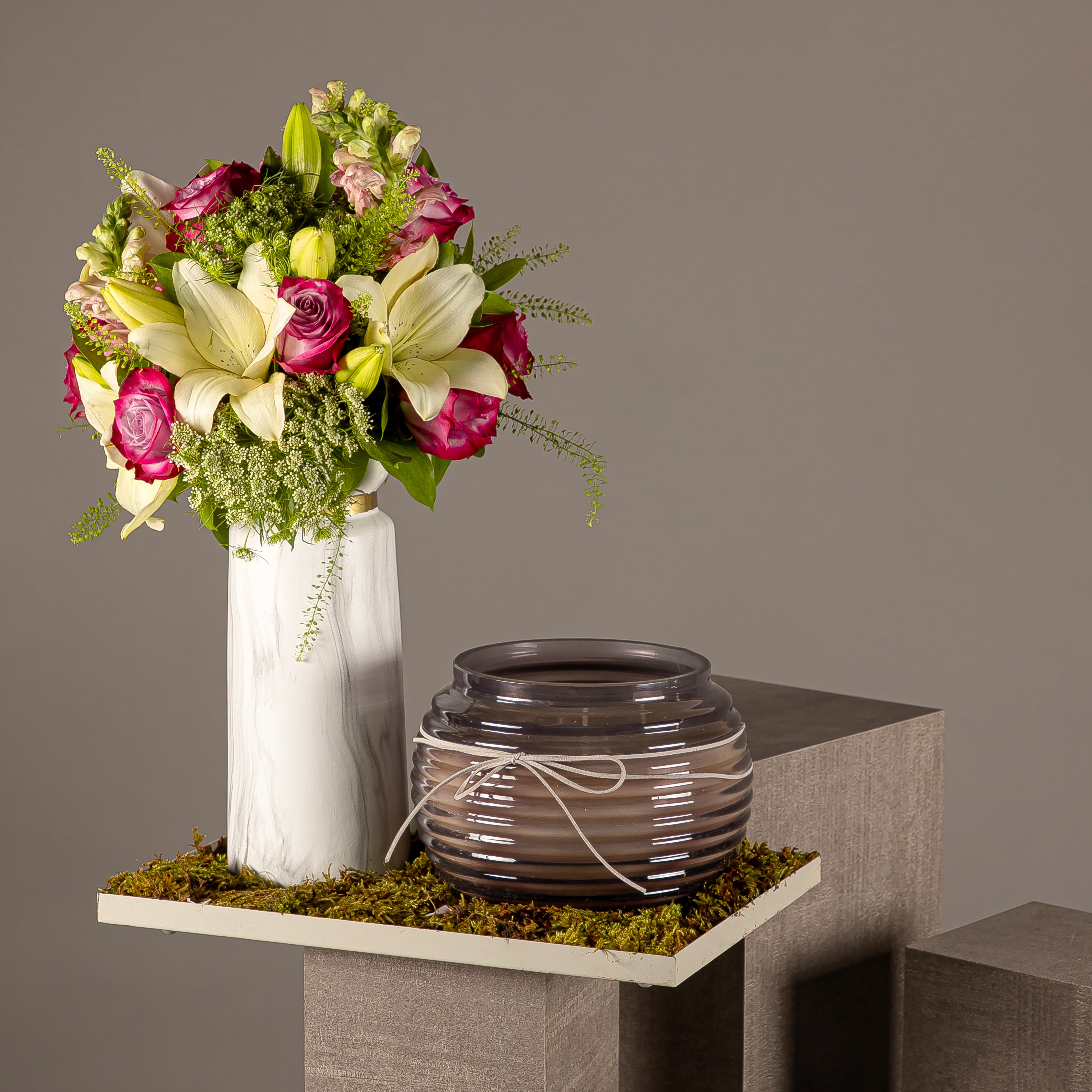 A tray with a flower vase of white lilies and pink roses, and a black glass candle