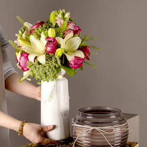 A tray with a flower vase of white lilies and pink roses, and a black glass candle