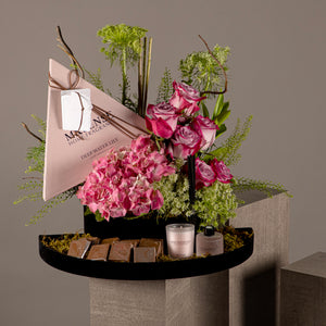 A chocolate tray with a box containing a diffuser and candle, decorated with various types of pink flowers