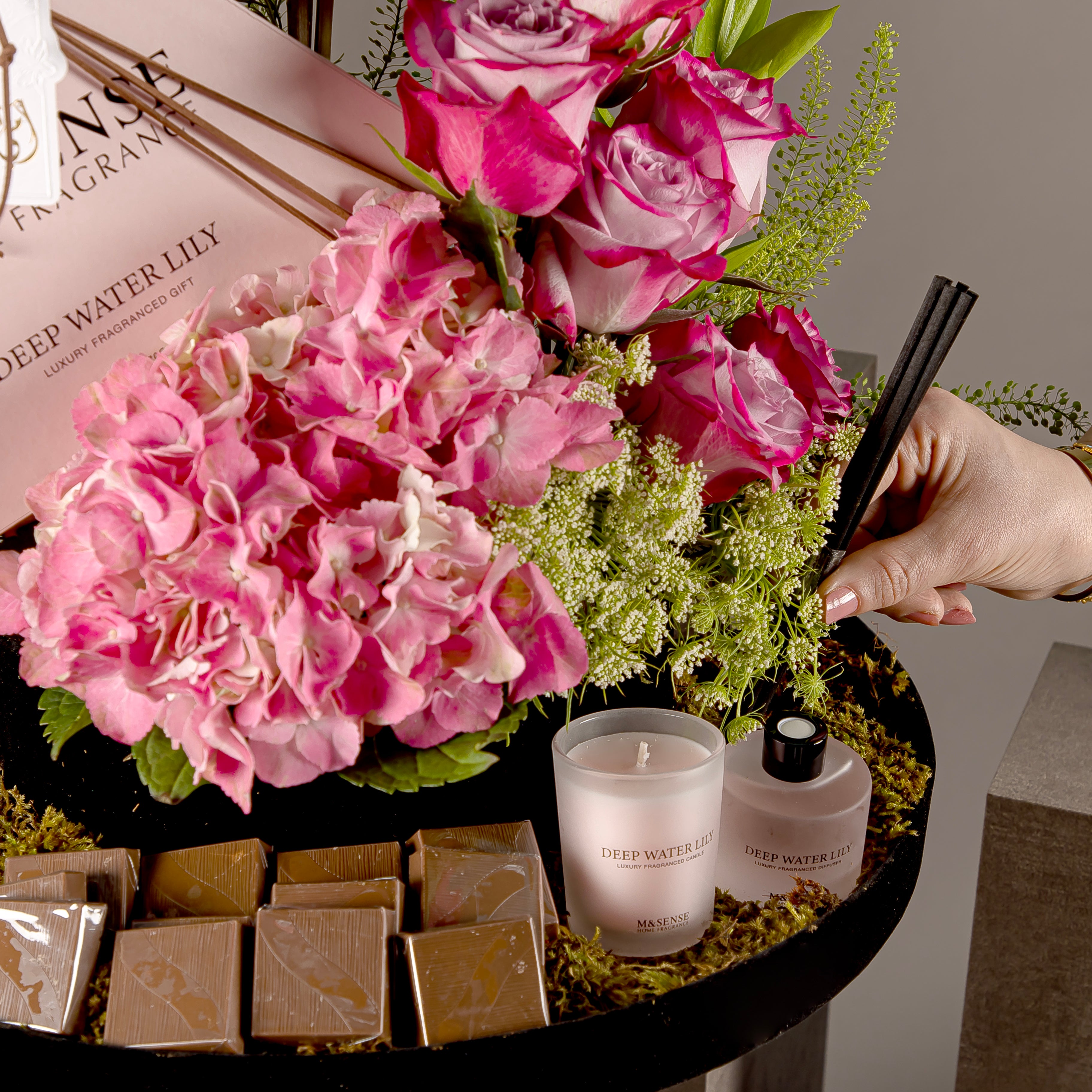 A chocolate tray with a box containing a diffuser and candle, decorated with various types of pink flowers